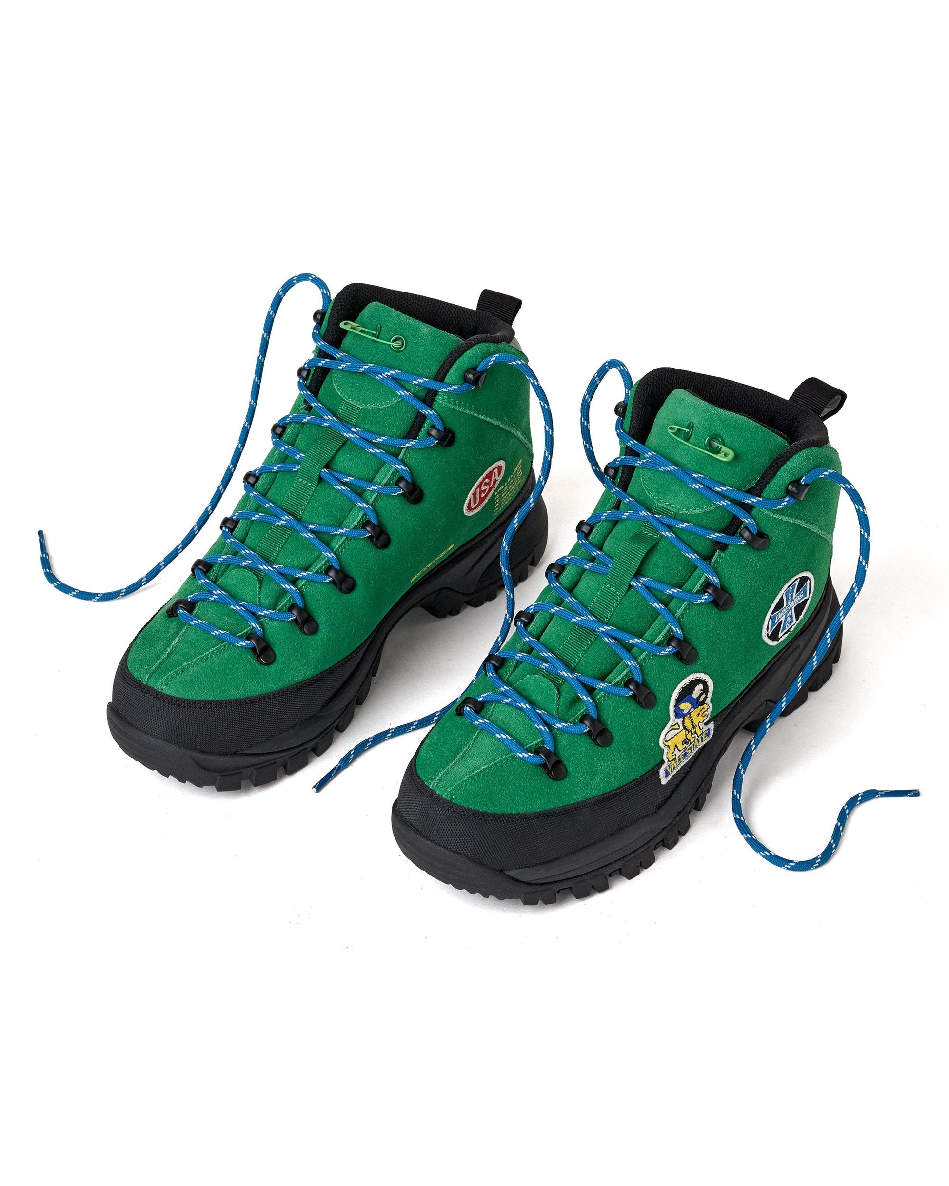 A pair of green high-top hiking boots with black soles and laces threaded through blue-and-black braided laces. The boots feature various patches on the sides.
